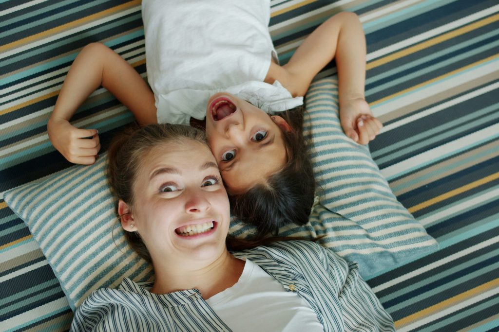 Mutter und Tochter liegen lächelnd auf gestreiften Kissen und zeigen Freude sowie Nähe zueinander, perfekt zur Buchung von Mutter-Tochter-Kursen.
