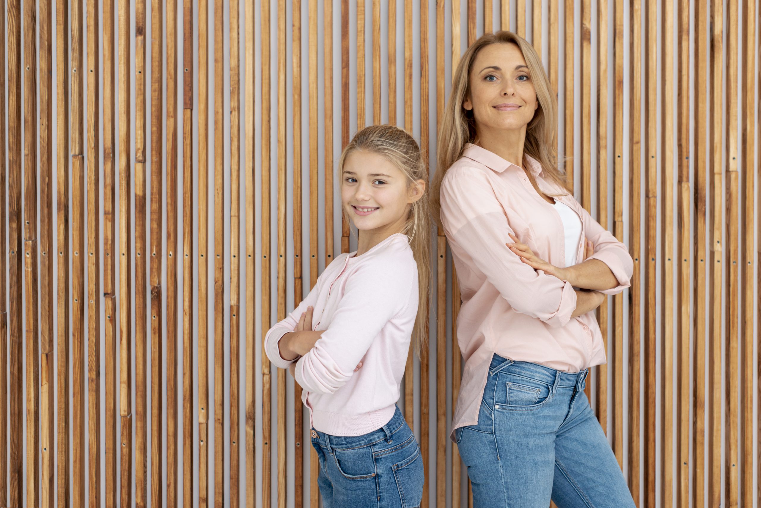 Mutter und Tochter stehen nebeneinander vor einer Wand mit überkreuzten Armen. Symbolisiert Mutter-Tochter-Kurse.